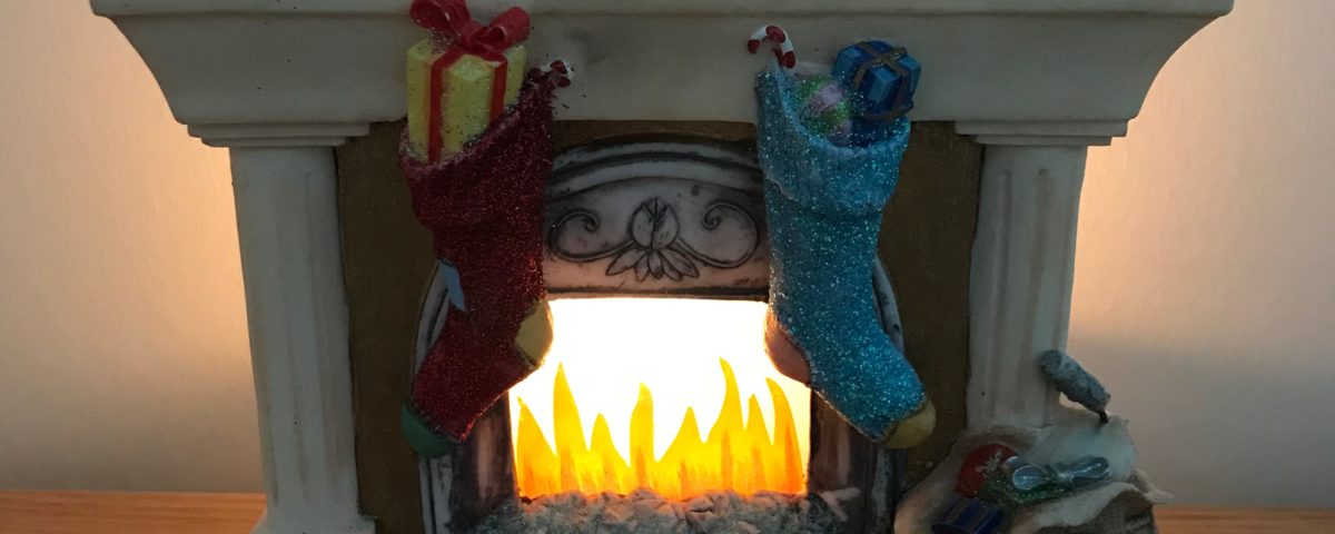 Pottery ornament of a fireplace all set with Christmas decorations, tea-light candle, stockings hung, clock on mantle piece